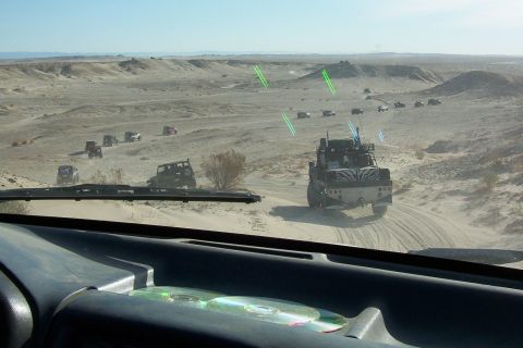 1995 Ford Bronco - A group of off-road vehicles traverses a sandy desert terrain under a clear sky.