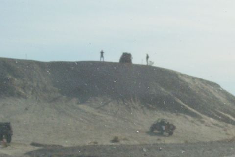 1995 Ford Bronco - Several people stand on a hill overlooking two vehicles in a sandy, outdoor environment.