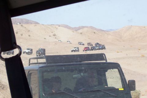 1995 Ford Bronco - A convoy of off-road vehicles navigates through a sandy, arid landscape under a clear sky.