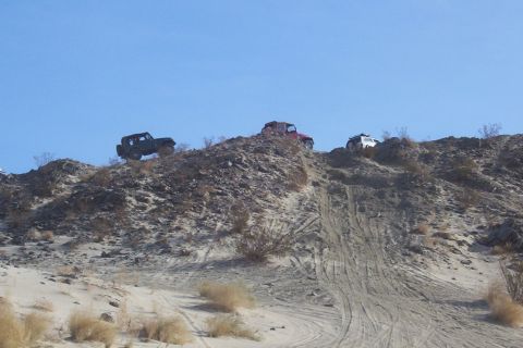 1995 Ford Bronco - Multiple off-road vehicles navigate a steep, sandy incline on a clear day.