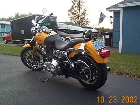 1998 Ford Crown Victoria - A yellow motorcycle is parked on an asphalt surface with a trailer and boat in the background.