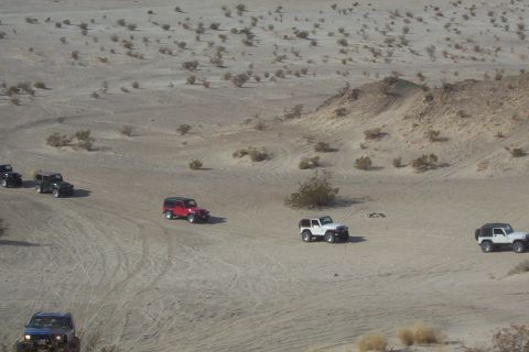 1995 Ford Bronco - Multiple Jeeps traverse a desert landscape, kicking up dust on the sandy trails.