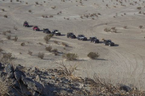 1995 Ford Bronco - A group of Jeeps travels across a dry, arid terrain under a clear sky.