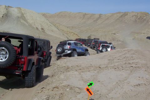 1995 Ford Bronco - Multiple off-road vehicles navigate sandy terrain under a clear sky.