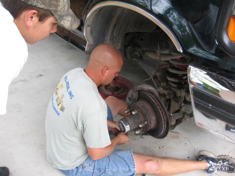 1974 Ford F-100 - Two men work on the front wheel hub of a dark green truck. The registry claims it is a 1974 Ford F-100, but the visual evidence is inconclu…