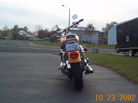 1998 Ford Crown Victoria - Yellow motorcycle parked on asphalt with houses and a trailer in the background.