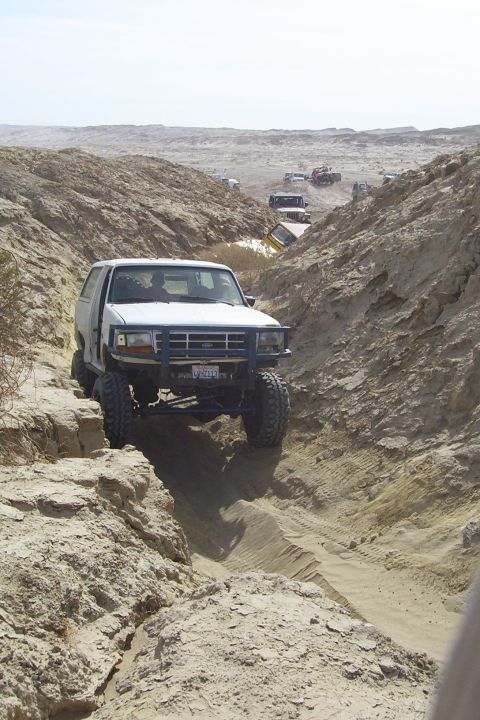 1995 Ford Bronco - Several vehicles navigate a steep, sandy canyon trail under a clear sky.