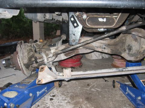 1974 Ford F-100 - Close-up view of the rear axle and suspension system of a vehicle being worked on, supported by hydraulic jacks.