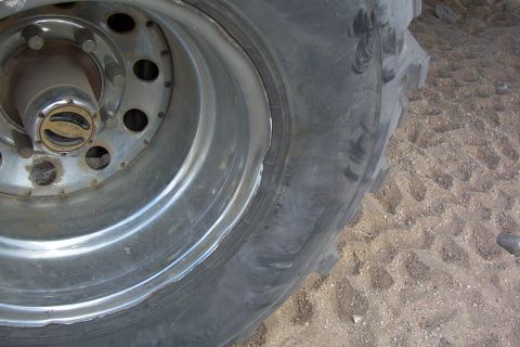 1995 Ford Bronco - A close-up view of a chrome wheel with a WARN locking hub and a large tire, set against a sandy background.