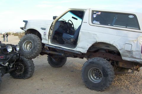 1995 Ford Bronco - Modified 1995 Ford Bronco with oversized tires is shown off-roading next to another vehicle.