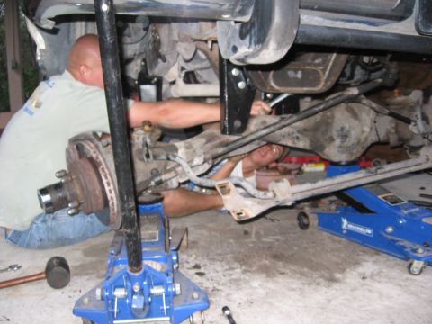 1974 Ford F-100 - Two mechanics are seen working on the undercarriage of a vehicle, which is supported by hydraulic jacks.