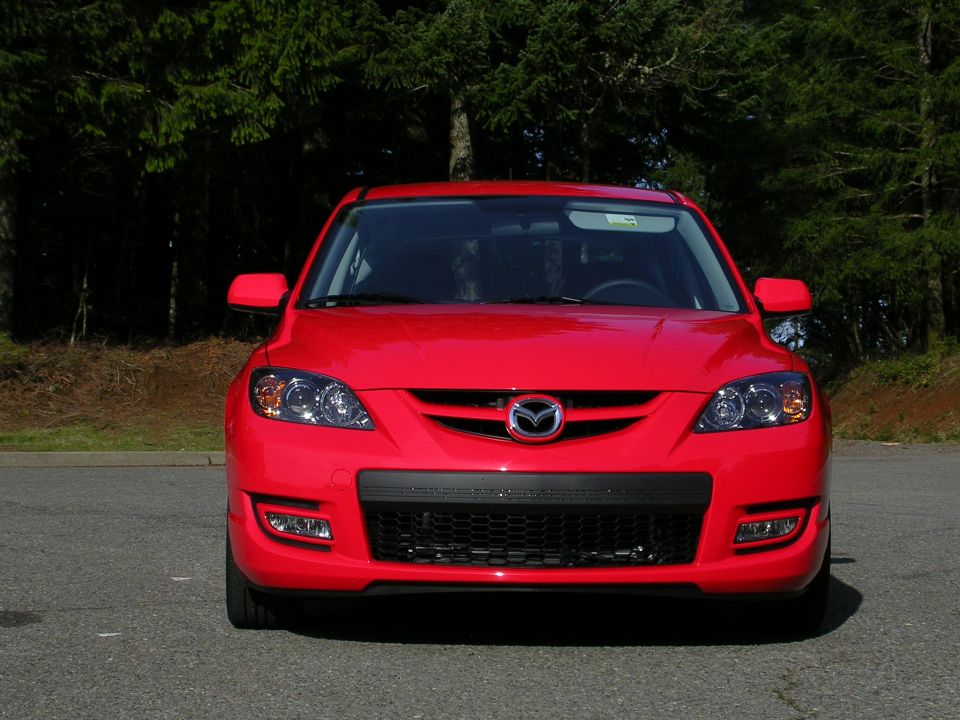 Red Mazda 3 front view showing Mazda badge, mesh lower grille and hood scoop