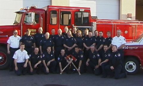 1998 Ford Crown Victoria - A group of firefighters stand and kneel in front of a large red fire truck.