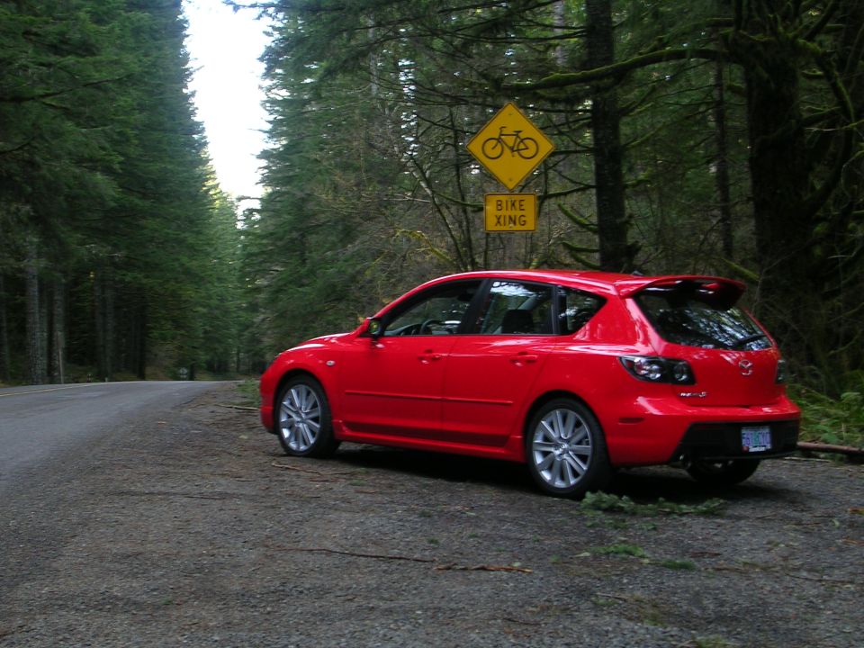 Red Mazda 3 hatchback parked on a forest road pullout under a bike crossing sign
