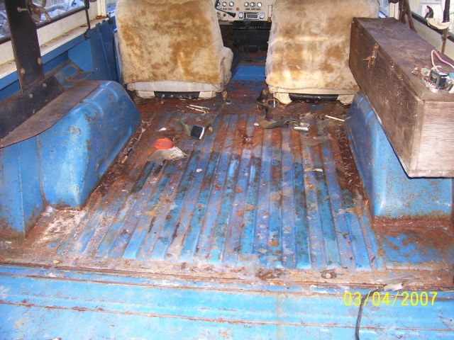 Rusty blue metal cargo floor and worn front seats inside a stripped 1973 Ford Bronco