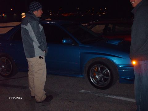 1995 Ford Probe - A blue Subaru WRX STI is parked at night, showing its distinctive hood scoop and orange brake calipers.