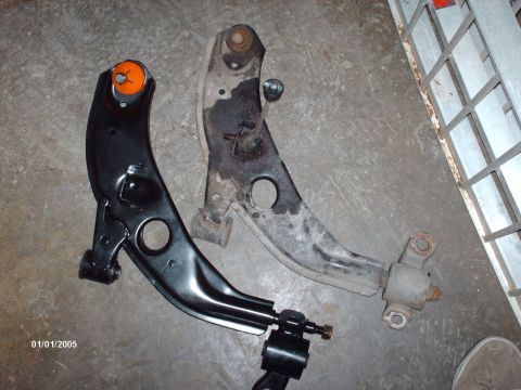1995 Ford Probe - A new black control arm is shown next to an old, worn-out control arm.