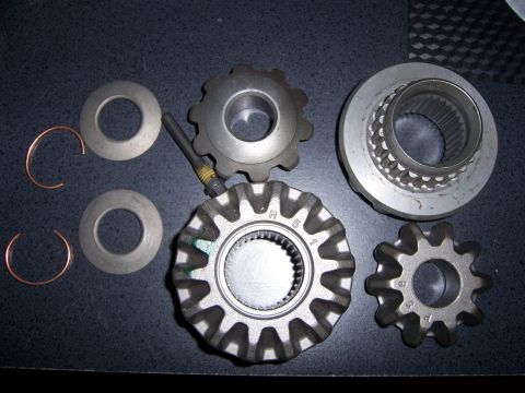 1991 Ford Bronco - Various metal gears and components for a vehicle's differential system are arranged on a dark, textured background.
