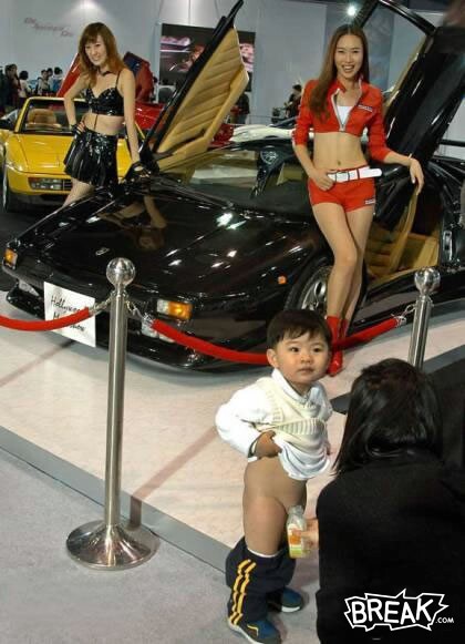 1991 Ford Bronco - A child stands in front of a black sports car at an auto show, with two women present.