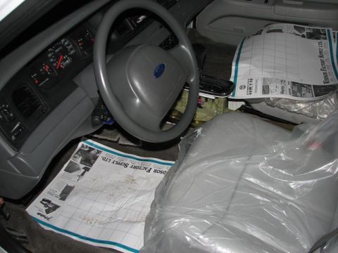 2003 Ford Crown Victoria - The interior of a 2003 Ford Crown Victoria is visible, with seats covered in protective plastic and newspapers on the floor.