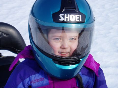 2000 Ford E350 - A child smiles while wearing a teal helmet and purple jacket, likely on a snowmobile in the snow.