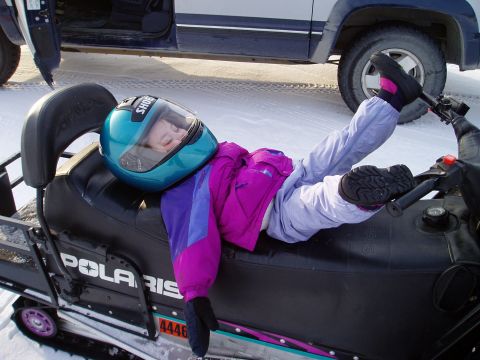 2000 Ford E350 - A person takes a nap on a snowmobile, with a vehicle nearby in a snowy landscape.