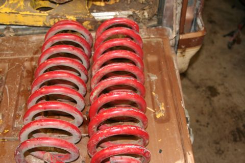 1989 Ford Bronco - Two sets of red coil springs are laid out on a wooden surface, possibly for a vehicle modification.