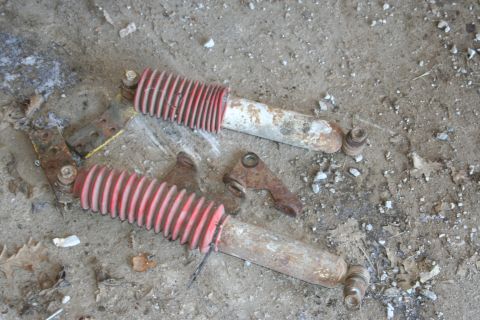1989 Ford Bronco - Two used lift kit shocks with red bellows and mounting brackets are shown on a dirt surface.