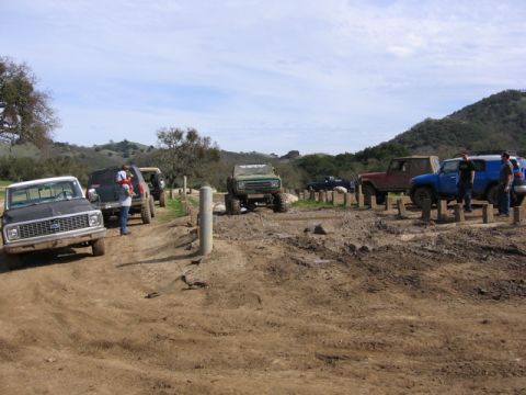 1989 Ford Bronco - A group of off-road vehicles navigate a muddy terrain under a partly cloudy sky.