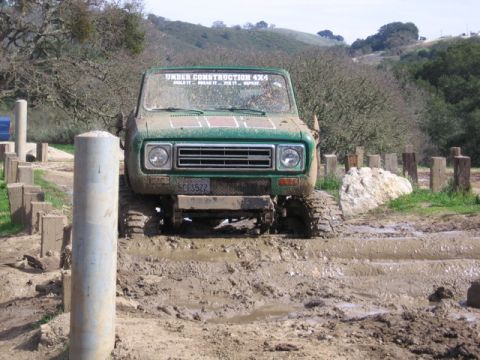 1989 Ford Bronco - Green International Scout II navigates a muddy obstacle course with "UNDER CONSTRUCTION 4X4" visible on the windshield.