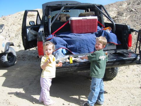 1992 Ford Bronco - Two children stand by the open tailgate of a black 1992 Ford Bronco, which is equipped with a roll cage and has a cooler and blankets in th…