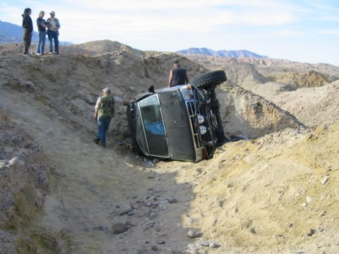 1992 Ford Bronco - An off-road vehicle has rolled over in a steep, sandy embankment, with onlookers observing the scene.