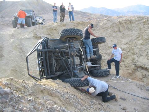 1992 Ford Bronco - Several people observe an overturned off-road vehicle in a sandy, hilly terrain.
