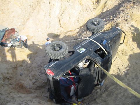 1992 Ford Bronco - A black 1992 Ford Bronco lies on its side, with a red Jeep nearby, as it is winched from a ditch.