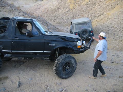 1992 Ford Bronco - Two off-road vehicles navigate a rocky, desert-like terrain with a man observing the scene.