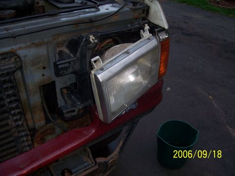 1990 Ford Bronco - The front end of a vehicle is shown with the headlight assembly removed, revealing internal components and some rust.