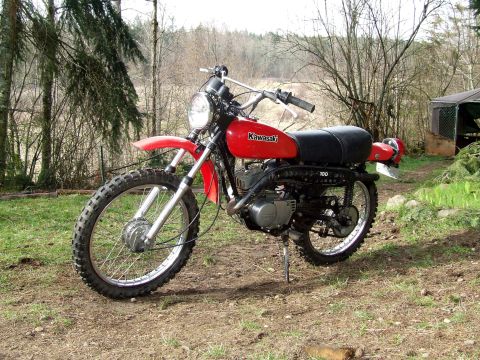 1997 BMW F650 - A red Kawasaki dirt bike with knobby tires is parked on a dirt path surrounded by trees.