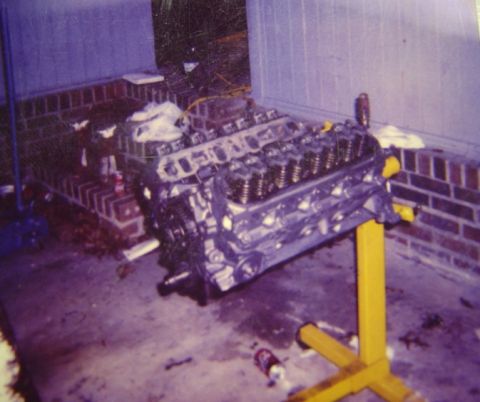 1986 Ford Bronco - Scanned film photo of a bare V8 engine block on a yellow engine stand in a garage, with the cylinder heads installed and valve covers off s…