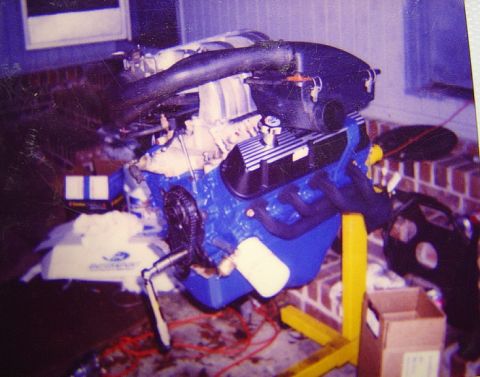 1986 Ford Bronco - Scanned film photo of a blue Ford V8 built up on a yellow engine stand in a garage, wearing black valve covers, an EFI upper intake plenum…