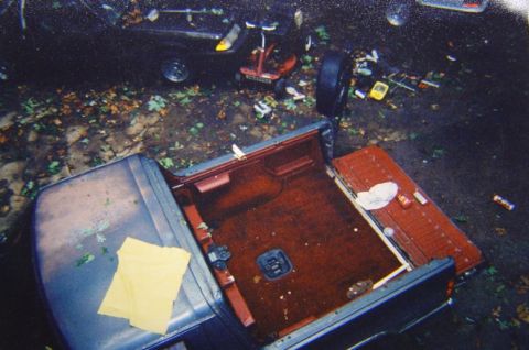 1986 Ford Bronco - A dark blue 1980s Ford Bronco's interior is visible with the tailgate open, parked outdoors with debris on the ground.