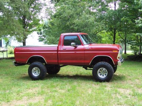 1974 Ford F-100 - This lifted pickup truck is parked on a grassy area with trees in the background.