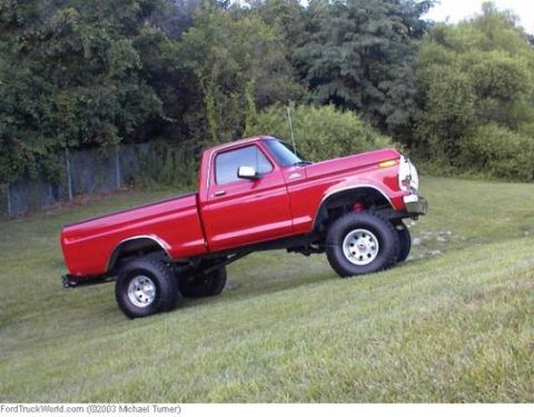 1974 Ford F-100 - A red pickup truck is parked on a grassy incline with trees in the background.