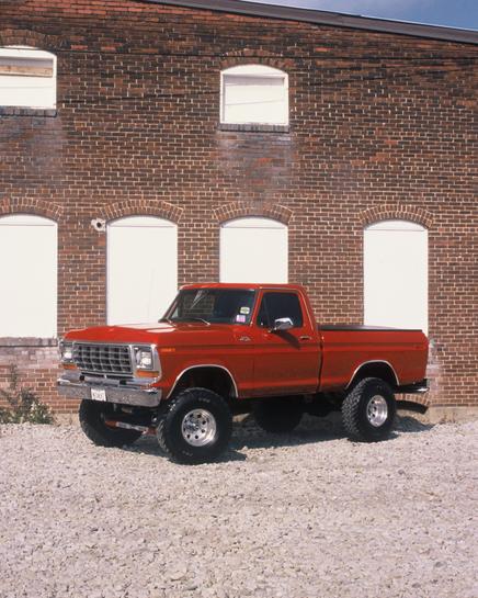 1974 Ford F-100 - A lifted red pickup truck is shown from a three-quarter front angle in front of a brick building.