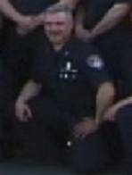 1998 Ford Crown Victoria - A man in a dark uniform kneels among other people.