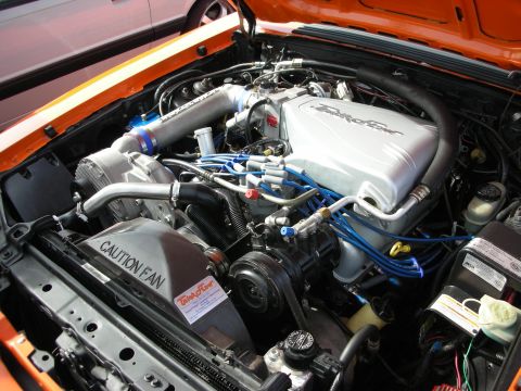 1998 Ford Crown Victoria - engine bay of an orange car showing a supercharged Ford V8 with blue spark plug wires and a 'CAUTION FAN' cover.