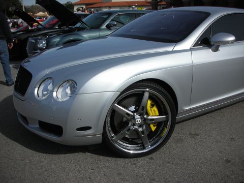 1998 Ford Crown Victoria - silver Bentley Continental GT at a car show, showing its quad headlights and a chrome multi-spoke wheel with yellow calipers.