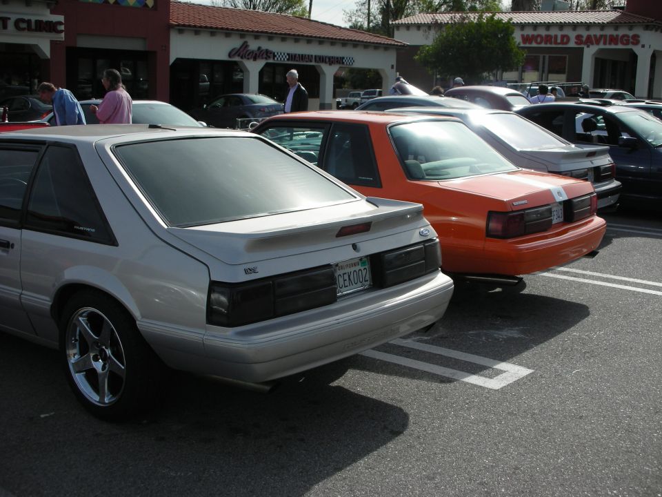 Silver and orange Fox-body Ford Mustang hatchbacks parked in a lot