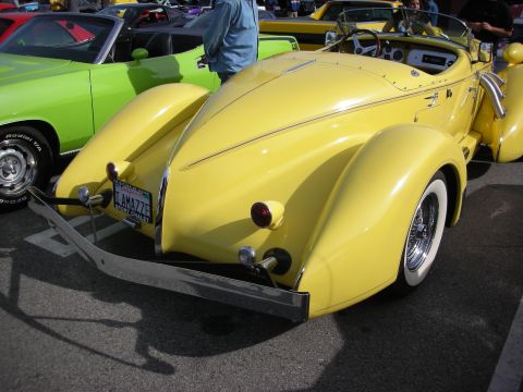 1998 Ford Crown Victoria - teardrop rear of a yellow boattail-style roadster with chrome bumper, dual taillights and whitewall wire wheels.