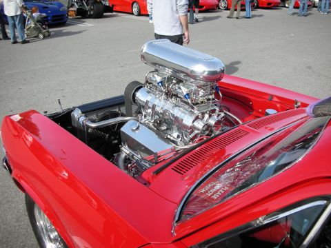 1998 Ford Crown Victoria - polished chrome supercharged V8 engine mounted in the bay of a red convertible at an outdoor car show.