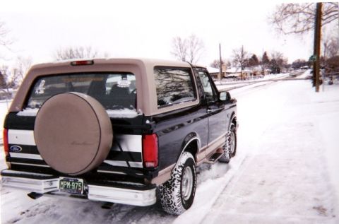 1996 Ford Bronco - Rear view of a 1996 Ford Bronco with a spare tire cover, parked on a snow-covered road.